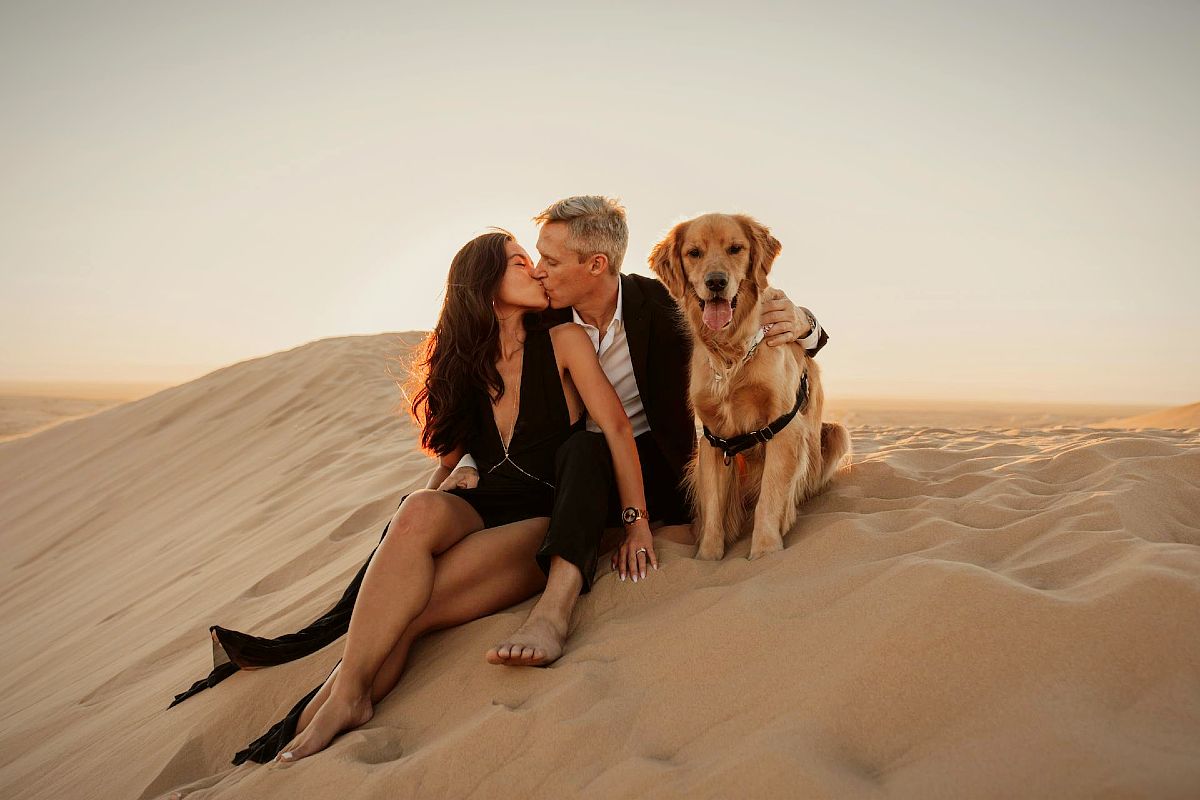 Casal feliz com um recetor dourado a beijar-se numa duna de areia